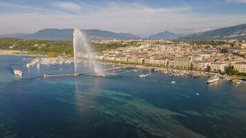 An aerial view of a coastal city with a prominent fountain, marina, and surrounding buildings.