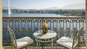 A balcony with a table and two chairs, overlooking a body of water with a fountain and boats.