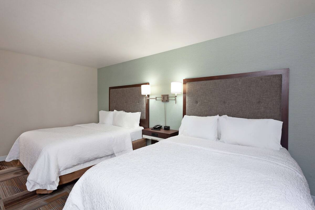 A hotel room with two beds, a nightstand, and a lamp.