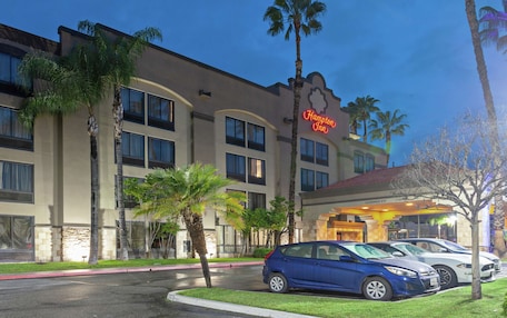 A hotel with a clear entrance, palm trees, and a parking area with cars.