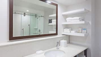 A bathroom with a large mirror, a sink, and shelves with towels.