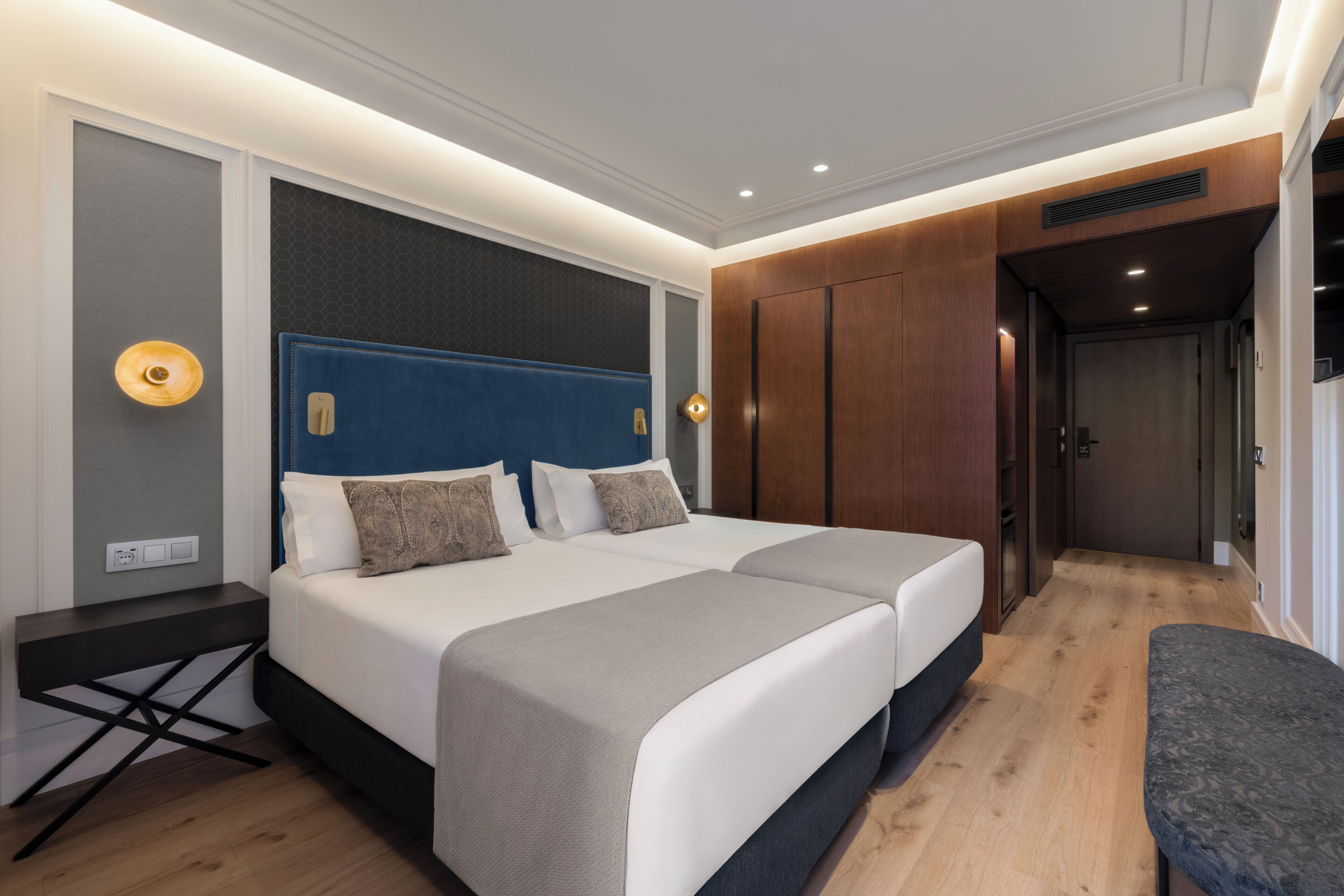 A modern hotel room with a large bed, bedside tables, a bench, and a wardrobe.