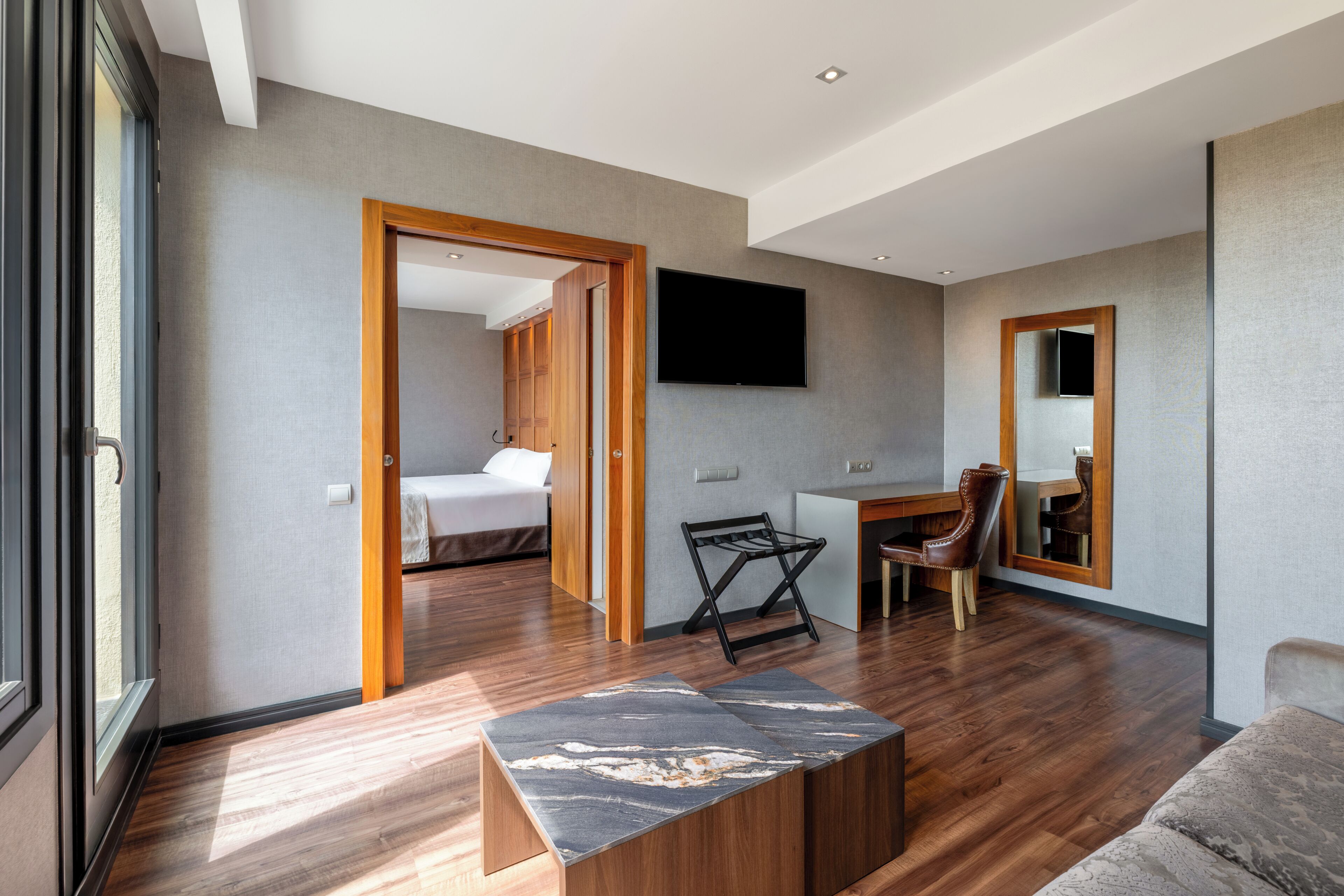 A modern hotel room with a bed, desk, chair, and a large mirror.