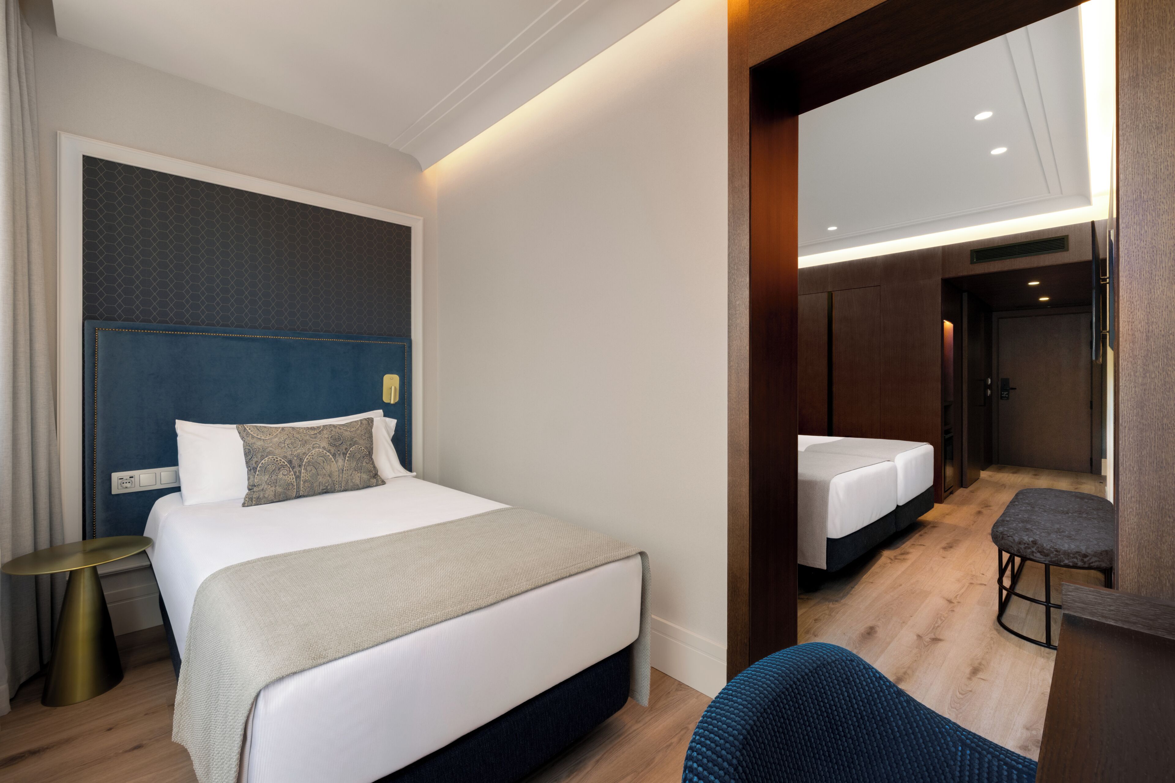 Quarto de hotel com uma cama grande, uma cama menor, área de estar e um espelho.