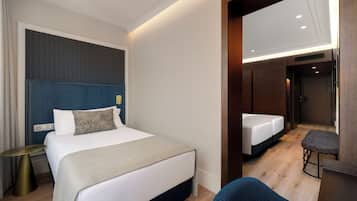 Quarto de hotel com uma cama grande, uma cama menor, área de estar e um espelho.