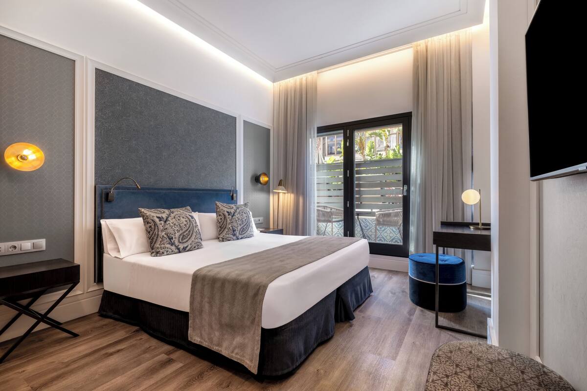 Quarto de hotel moderno com uma cama grande, uma mesa, uma cadeira, uma televisão e uma varanda com vista.