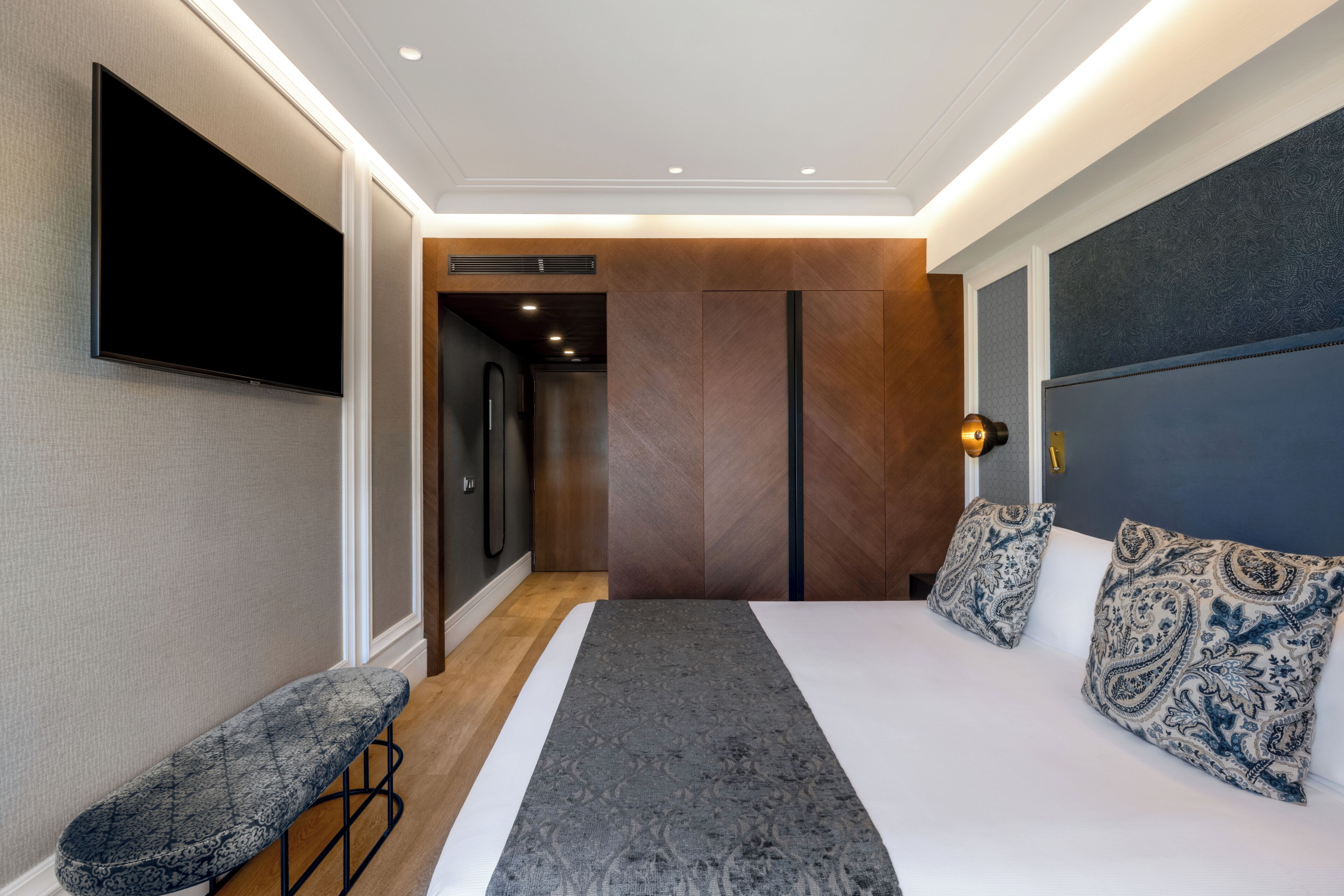 Quarto de hotel moderno com uma cama grande, um banco, televisão de tela plana e um guarda-roupa.