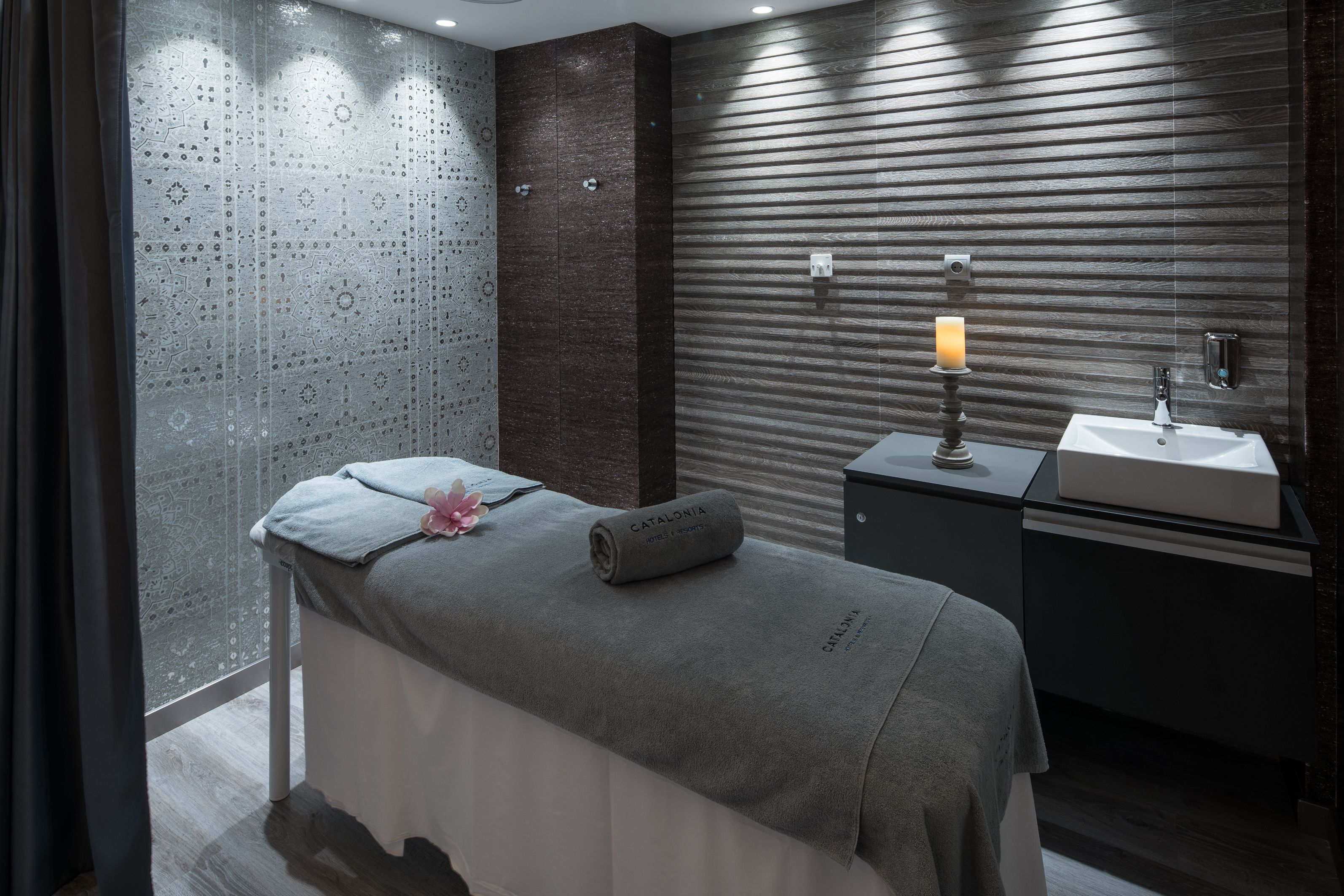 Ett modernt sparum med ett massagebord, ett litet handfat och ett dekorativt ljus.