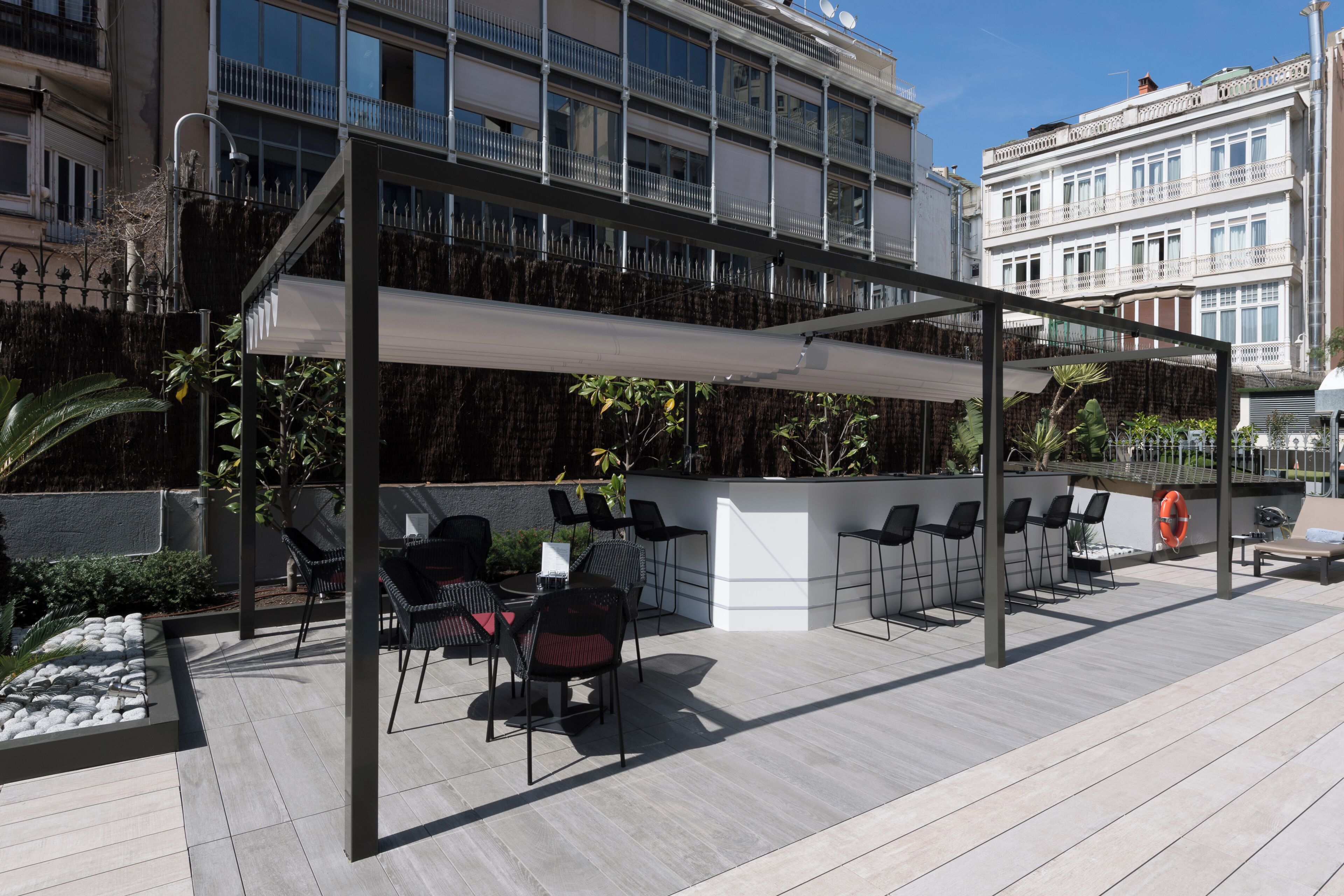 An outdoor seating area with tables and chairs, a covered section, and a view of a building with balconies.