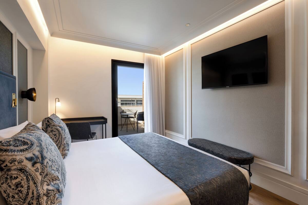 Quarto de hotel com cama, escrivaninha, cadeira, televisão e vista para a cidade.