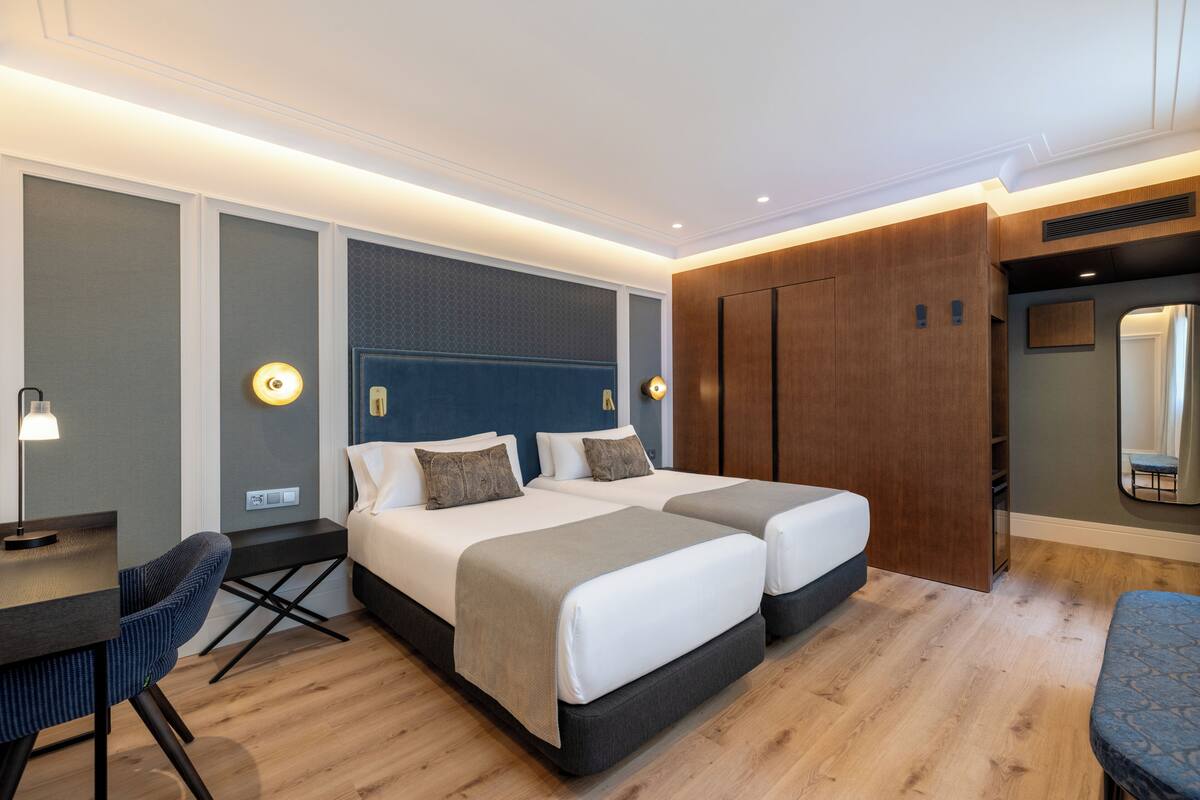 Quarto de hotel com cama, mesas de cabeceira, escrivaninha e uma cadeira.