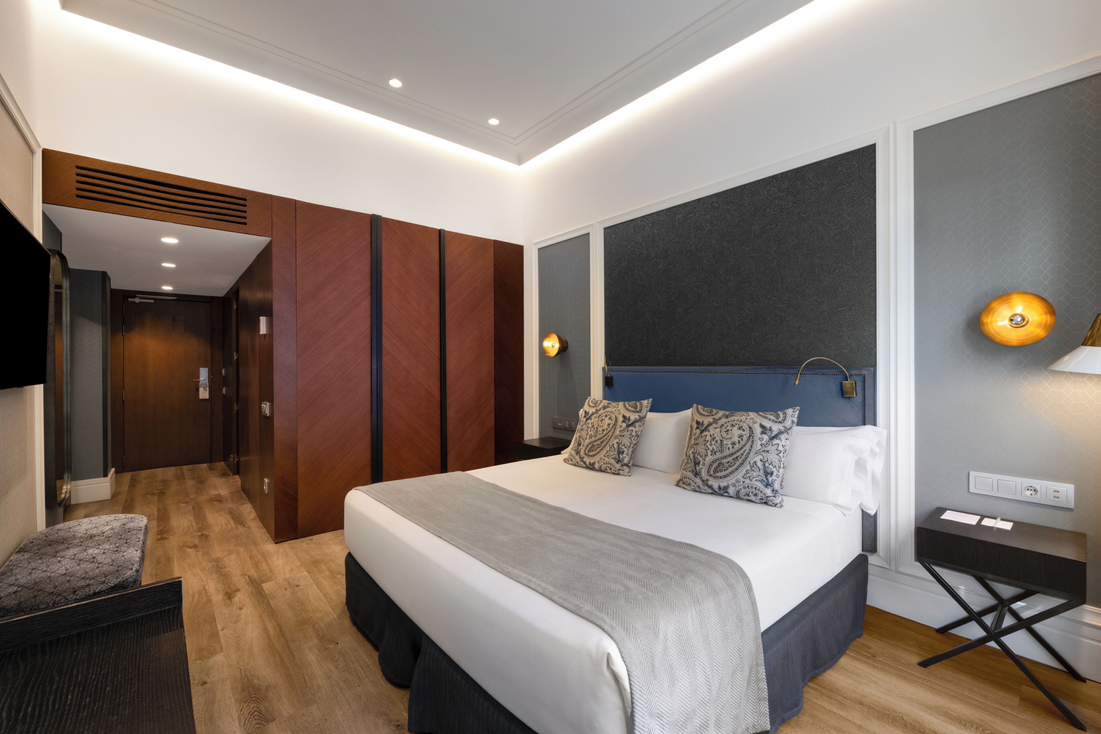 A modern hotel room with a large bed, a desk, and a TV.