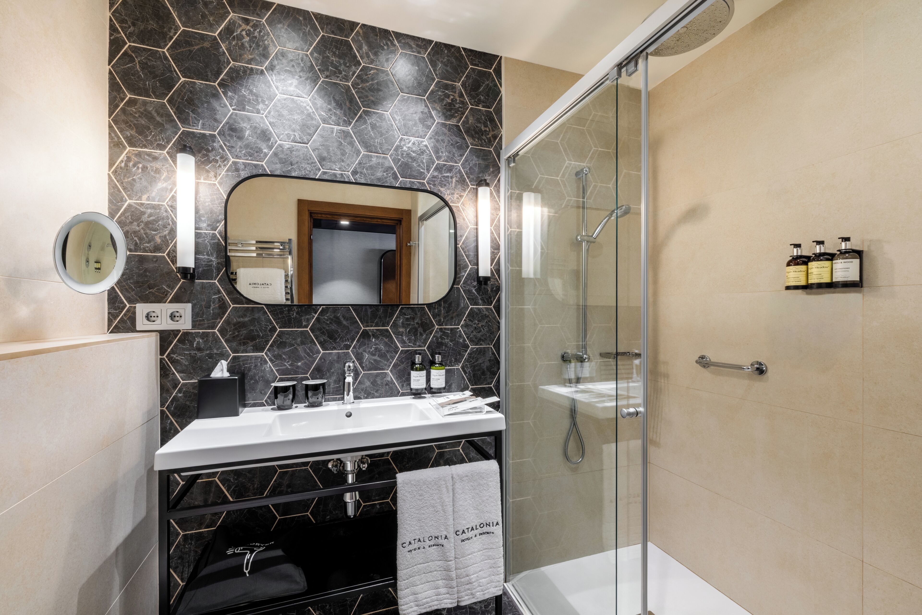 A modern bathroom with a glass-enclosed shower, a vanity with a mirror, and toiletries on the wall.