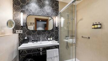 A modern bathroom with a glass-enclosed shower, a vanity with a mirror, and toiletries on the wall.