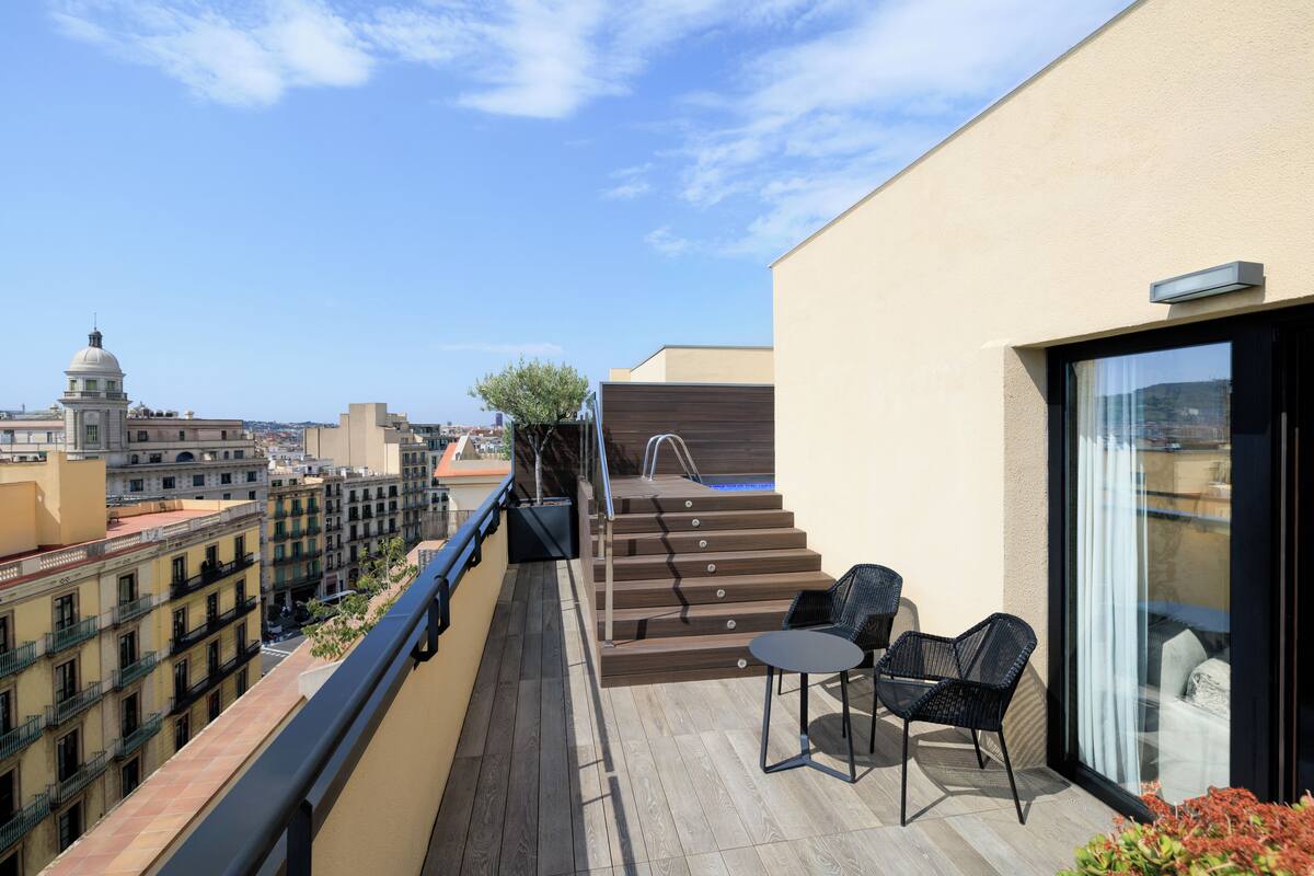 Terraço no telhado com escada de madeira, duas cadeiras e uma porta de vidro.