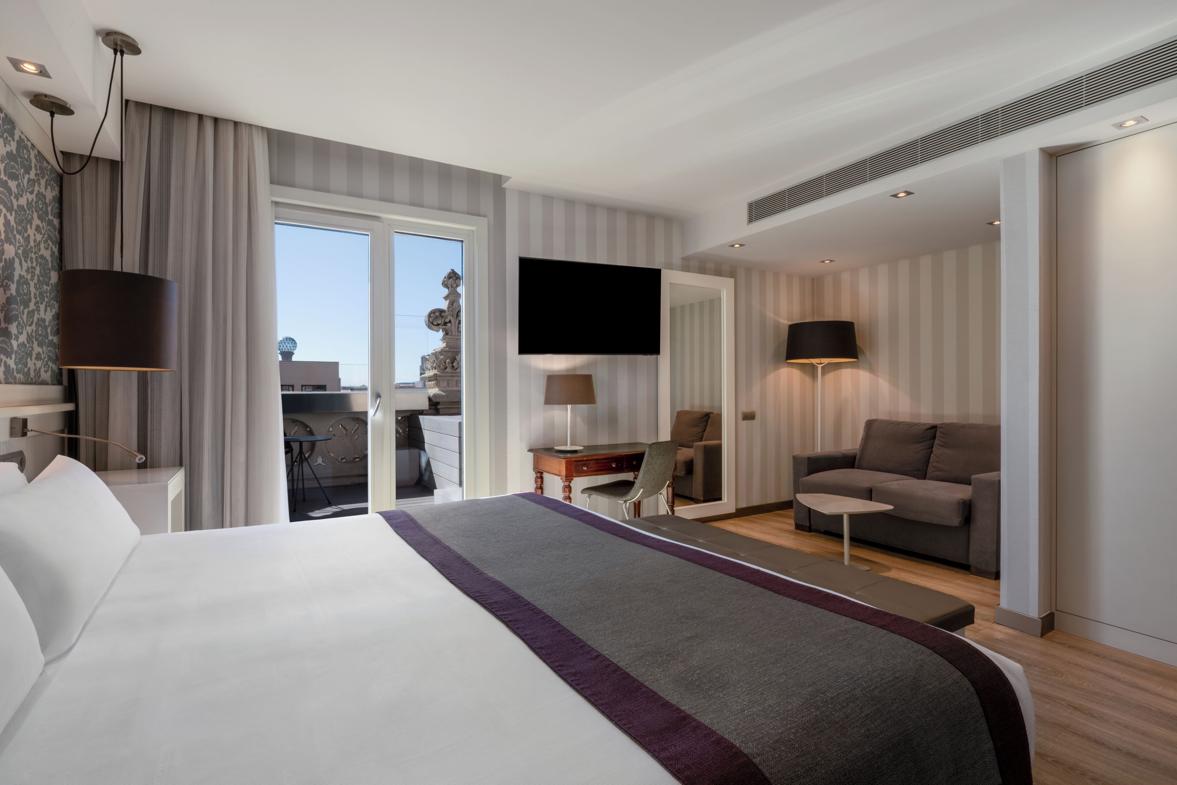 Una habitación de hotel moderna con una cama grande, un escritorio, un sofá y un televisor.