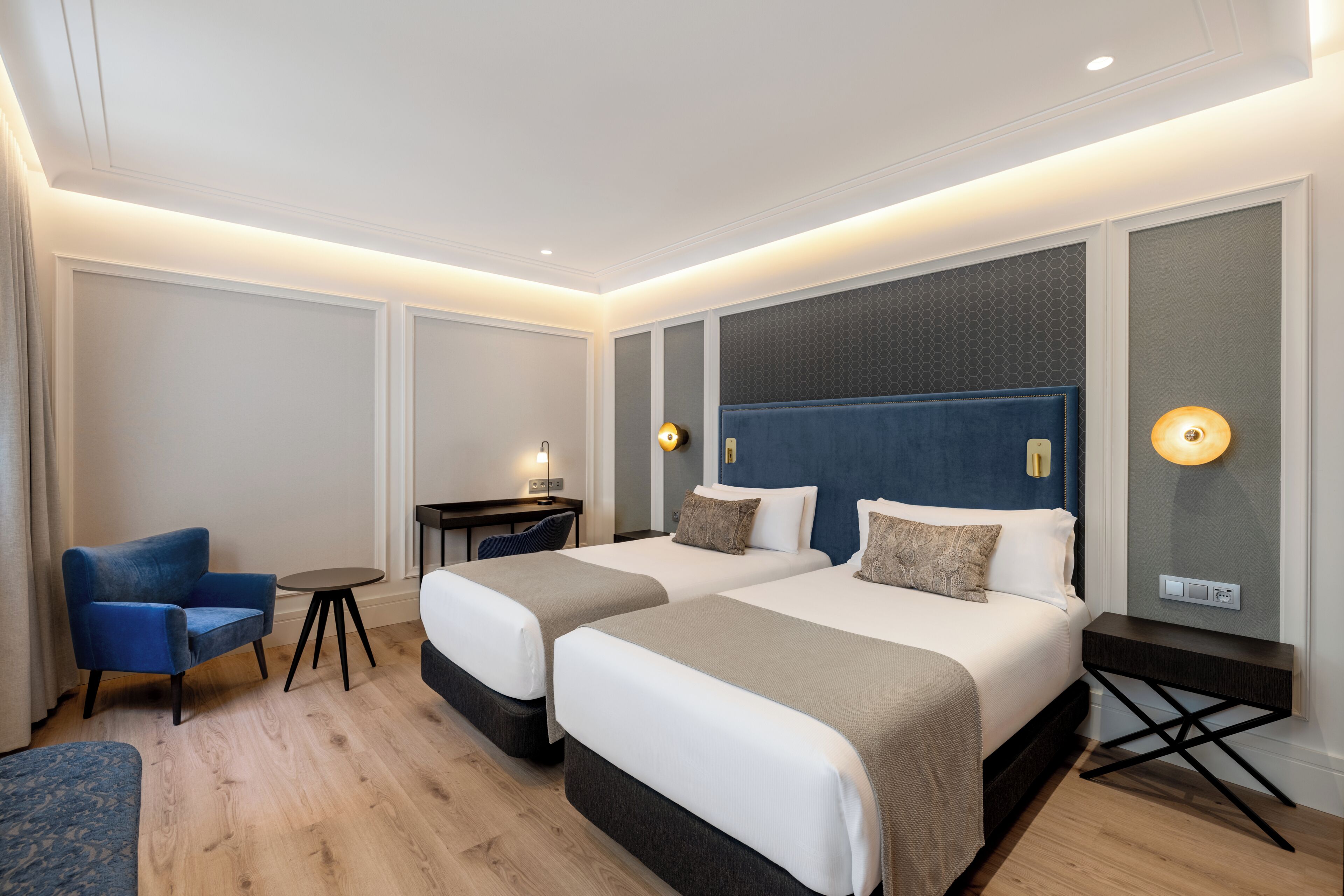 A hotel room with two beds, a desk, a chair, and a small table.
