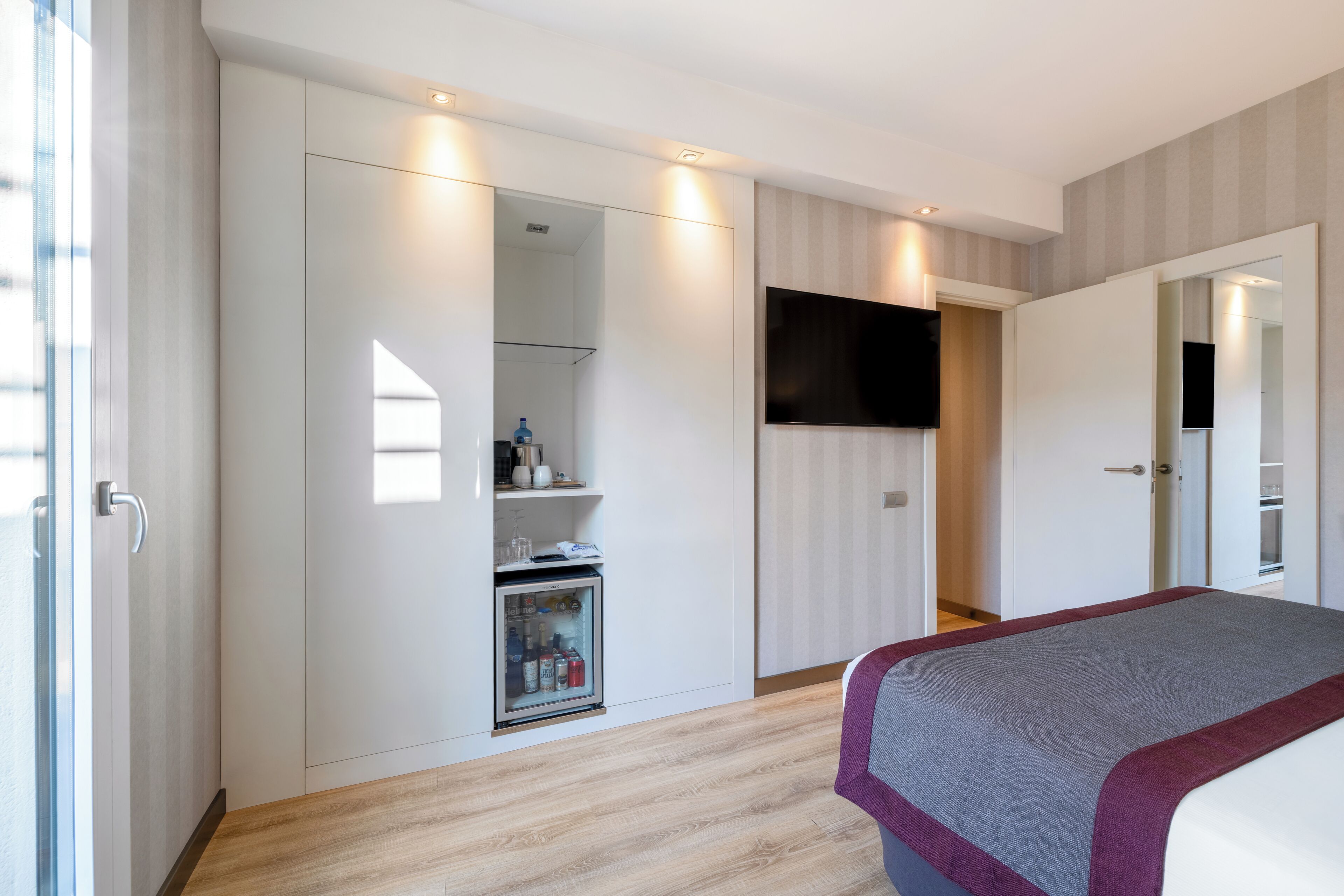 A bedroom with a bed, a wardrobe, a television, and a mini-fridge.