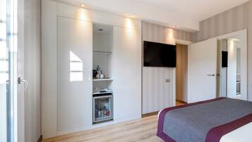 A bedroom with a bed, a wardrobe, a television, and a mini-fridge.