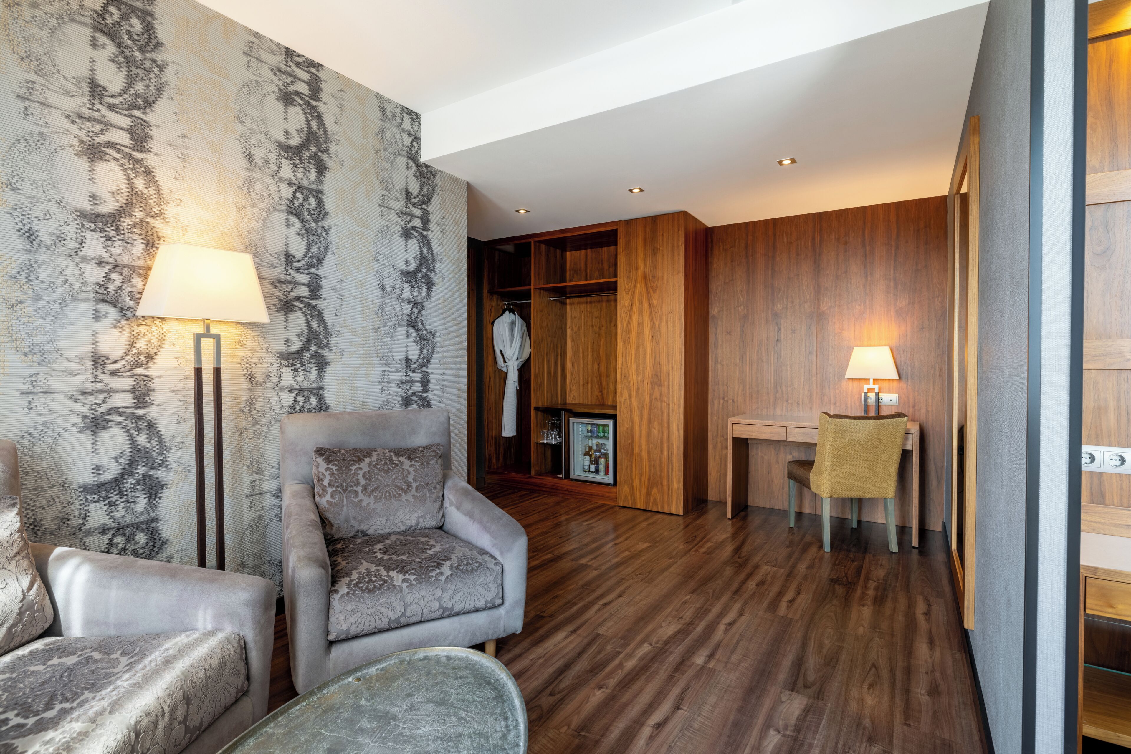 Moderni hotellihuone, jossa on sohva, nojatuoli ja pieni ruokapöytä tuoleineen.
