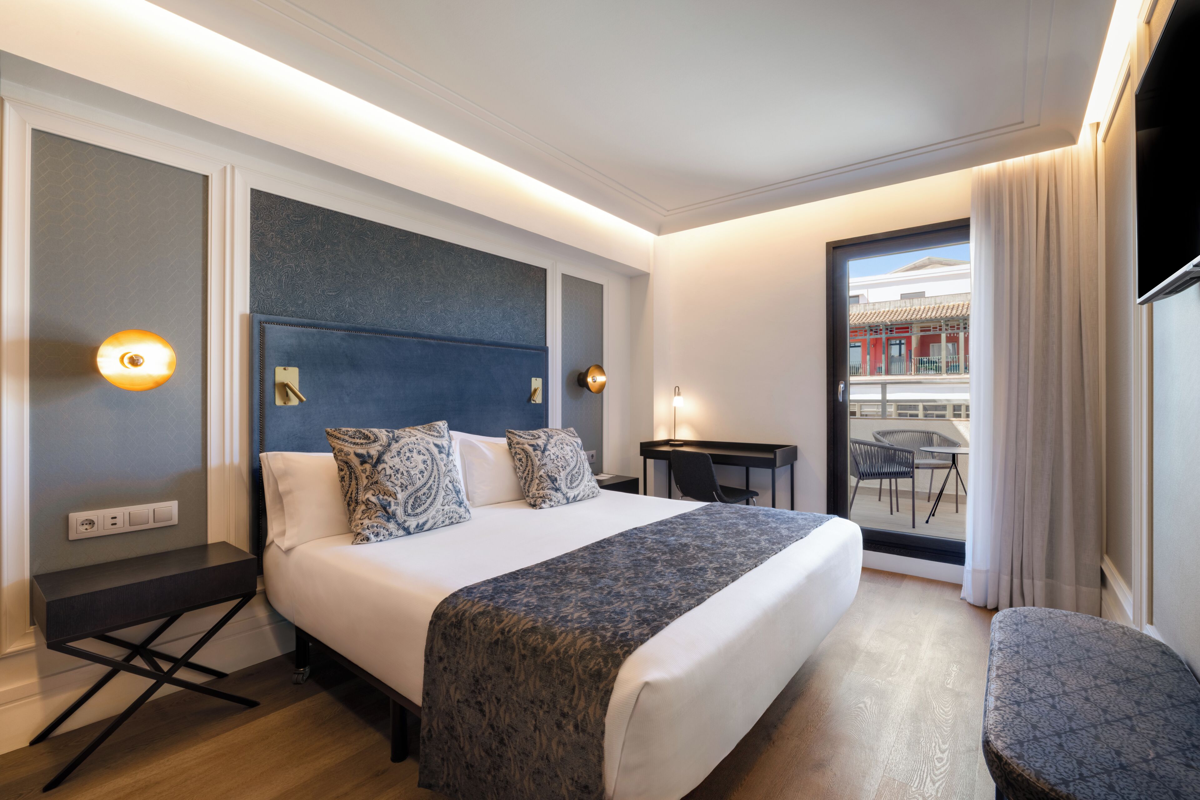 A hotel room with a large bed, bedside tables, a desk, and a balcony with a view.