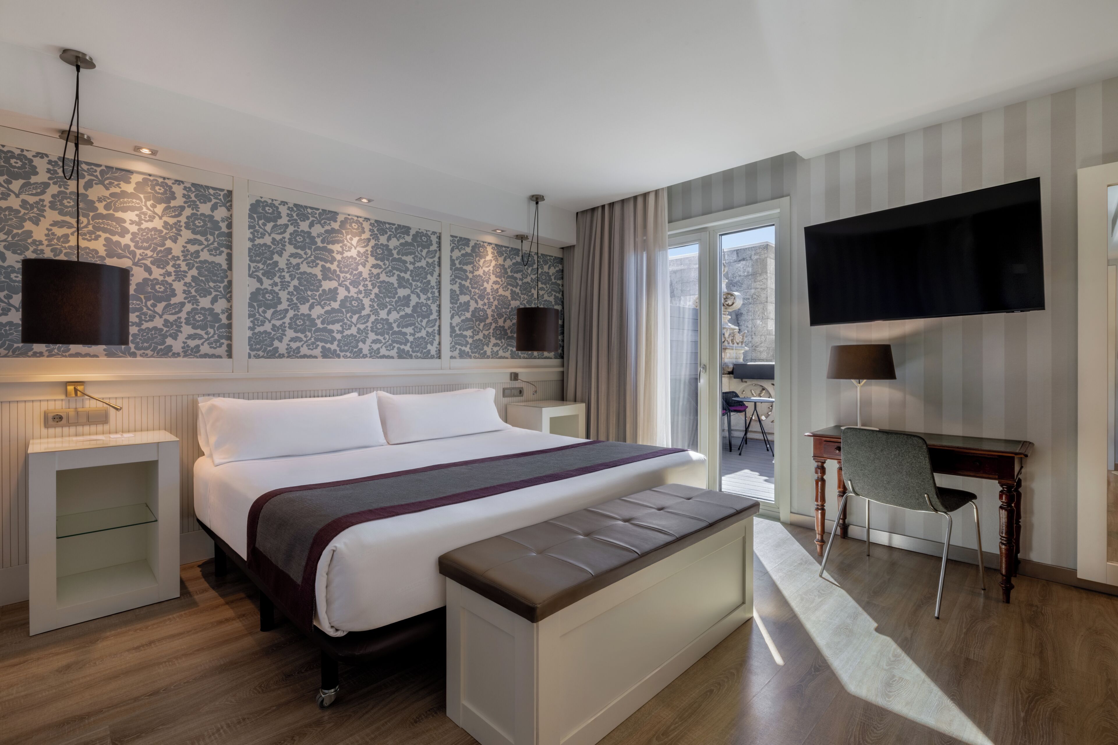 Hotelkamer met een groot bed, een bureau, een stoel, een aan de muur bevestigde televisie en een raam met gordijnen.