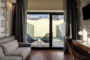 Moderni hotellihuone, jossa on sohva, ruokapöytä, tuoli, näkymä uima-altaalle ja seinälle asennettu televisio.