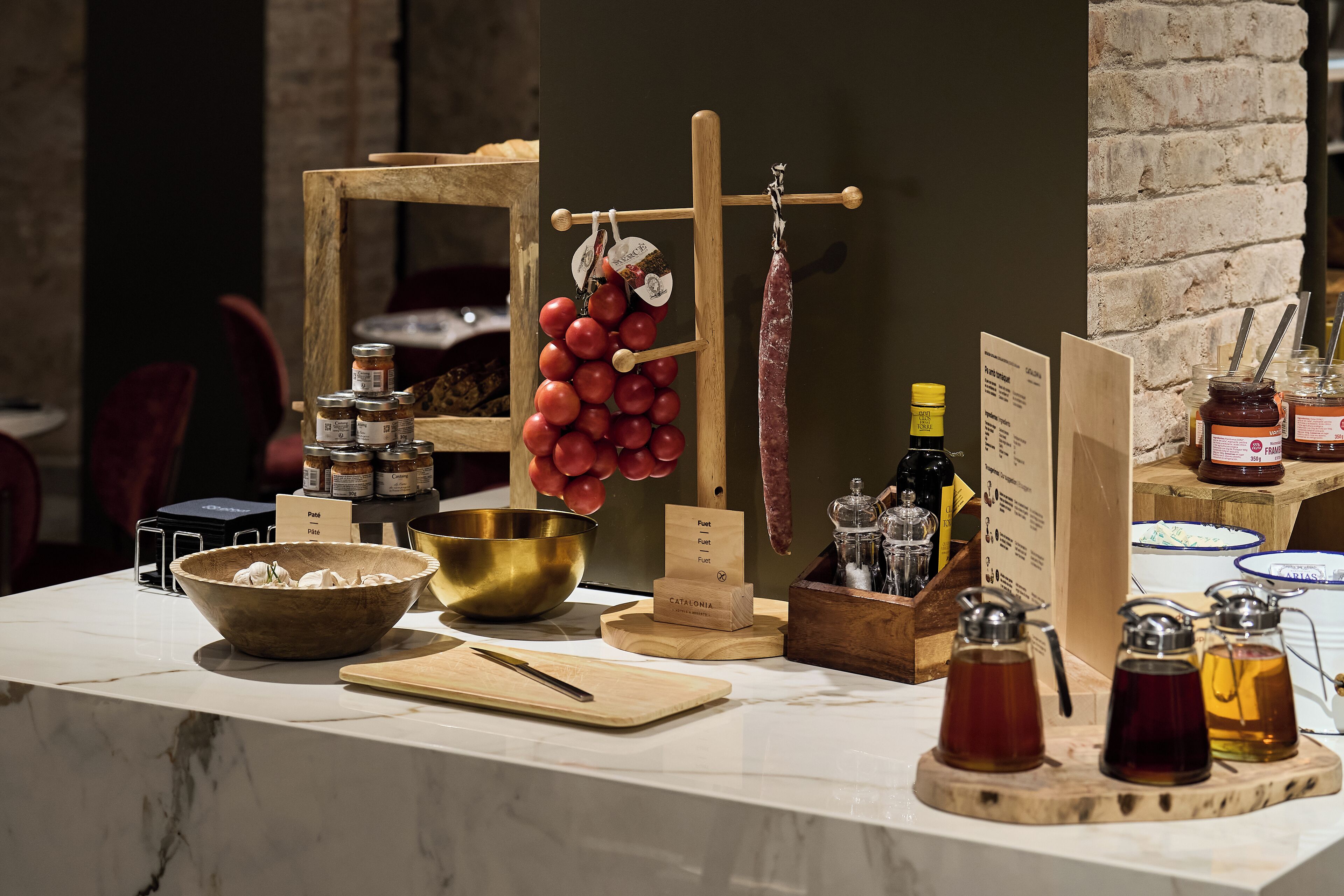 Una encimera de cocina con diversos alimentos, incluyendo un cuenco de madera, frascos, un colgador para tomates y una tabla de cortar de madera.