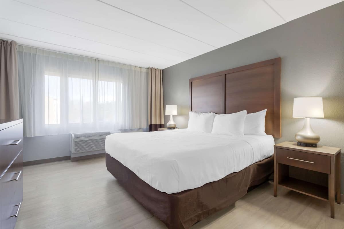 A hotel room with a large bed, bedside tables with lamps, a dresser, and a window with curtains.