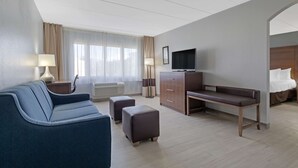 A hotel room with a sofa, ottoman, desk, TV, and a bed.