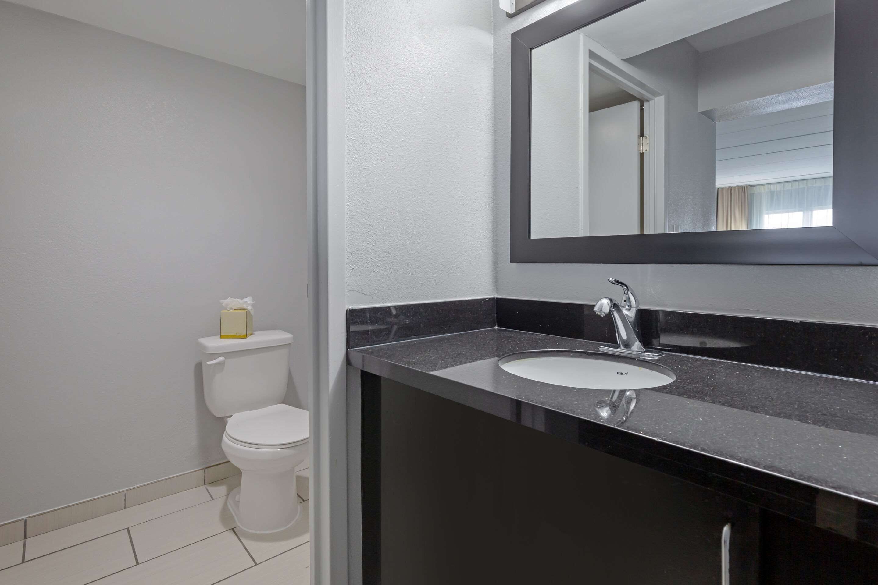 Un baño moderno con inodoro blanco, lavamanos negro y un espejo grande sobre el lavamanos.