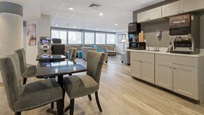 A modern hotel room with a dining area, a kitchenette, and an ATM.