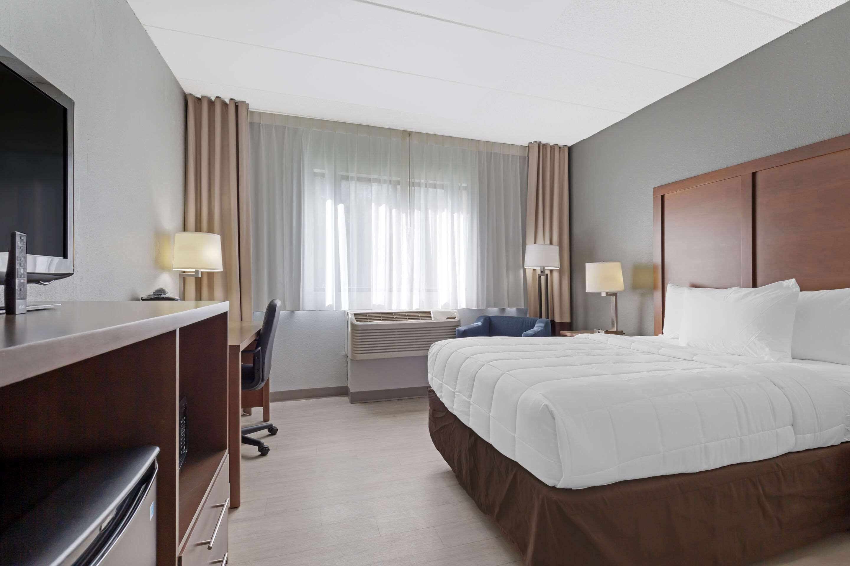 Ein Hotelzimmer mit Bett, Schreibtisch, Stuhl, Fernseher und zwei Lampen.