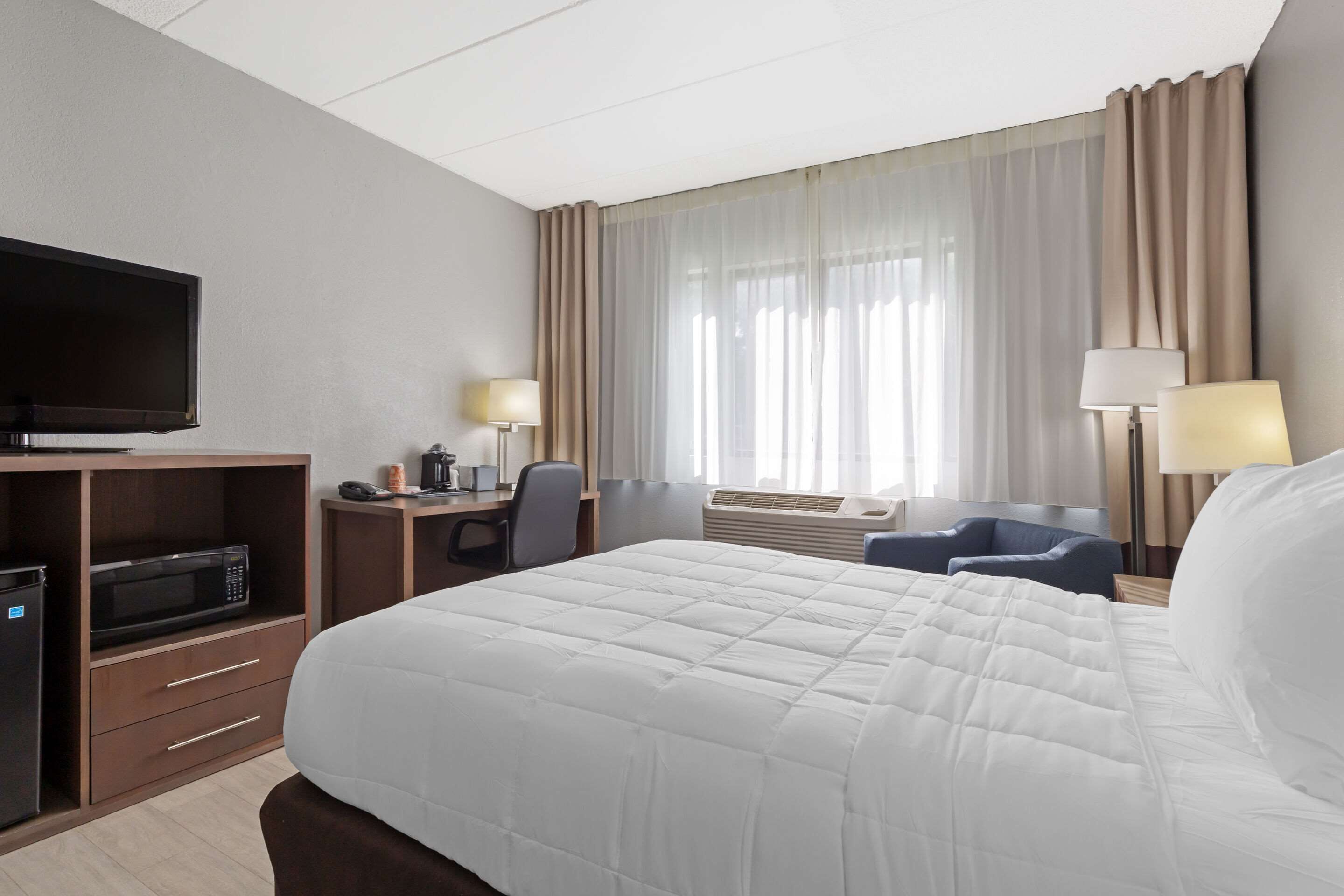 A hotel room with a large bed, a desk with a chair, a television, and a window with curtains.