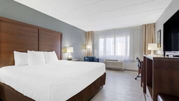 Quarto de hotel com uma cama grande, uma escrivaninha, uma cadeira, uma televisão e uma janela com cortinas.