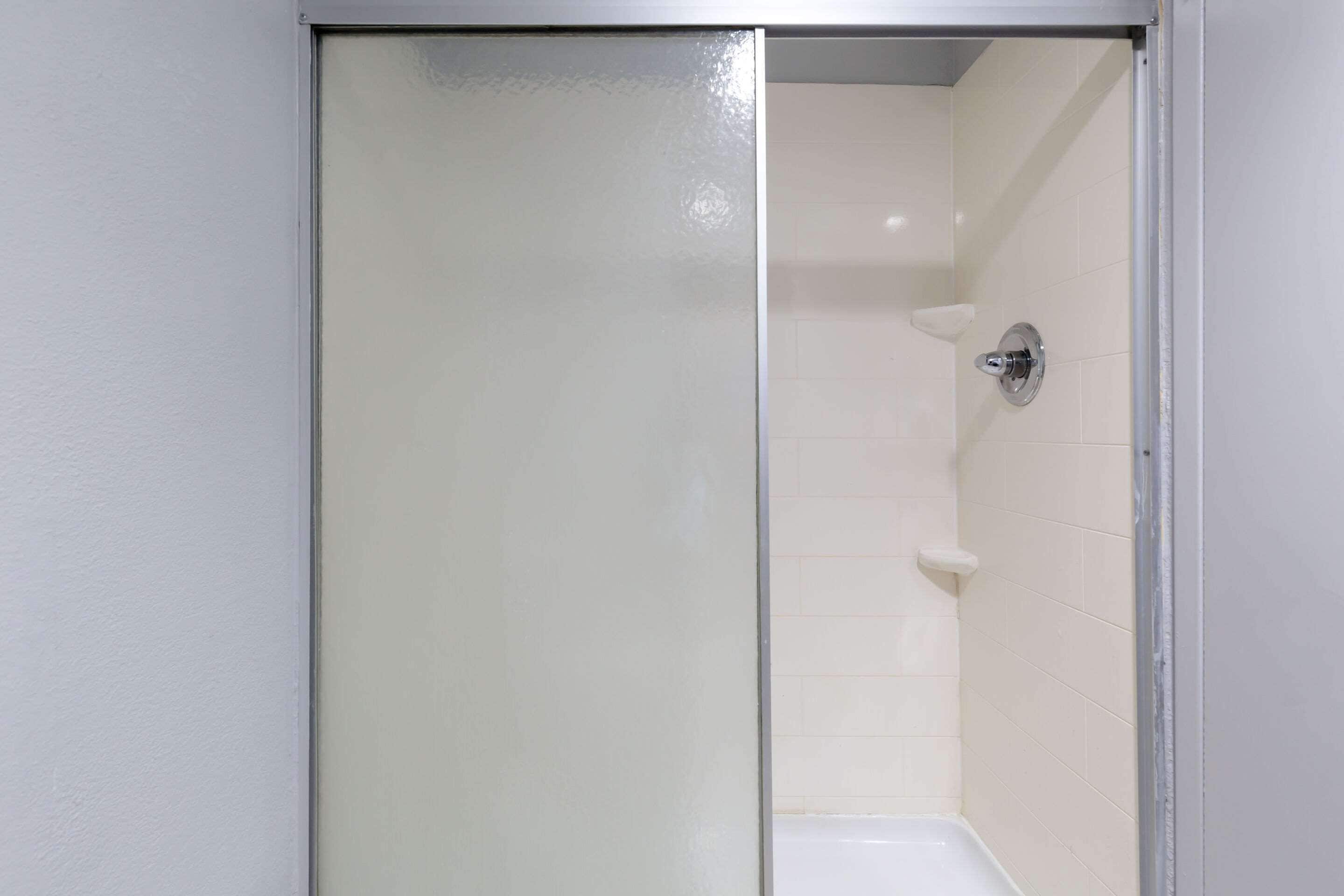 A shower with a glass door, white tiled walls, and a chrome faucet.