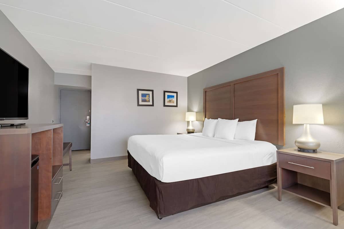 A hotel room with a large bed, bedside tables with lamps, a desk with a flat-screen TV, and two framed pictures on the wall.