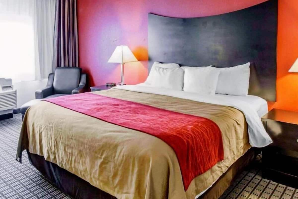 A hotel room with a large bed, a desk, a chair, a lamp, and a window with curtains.