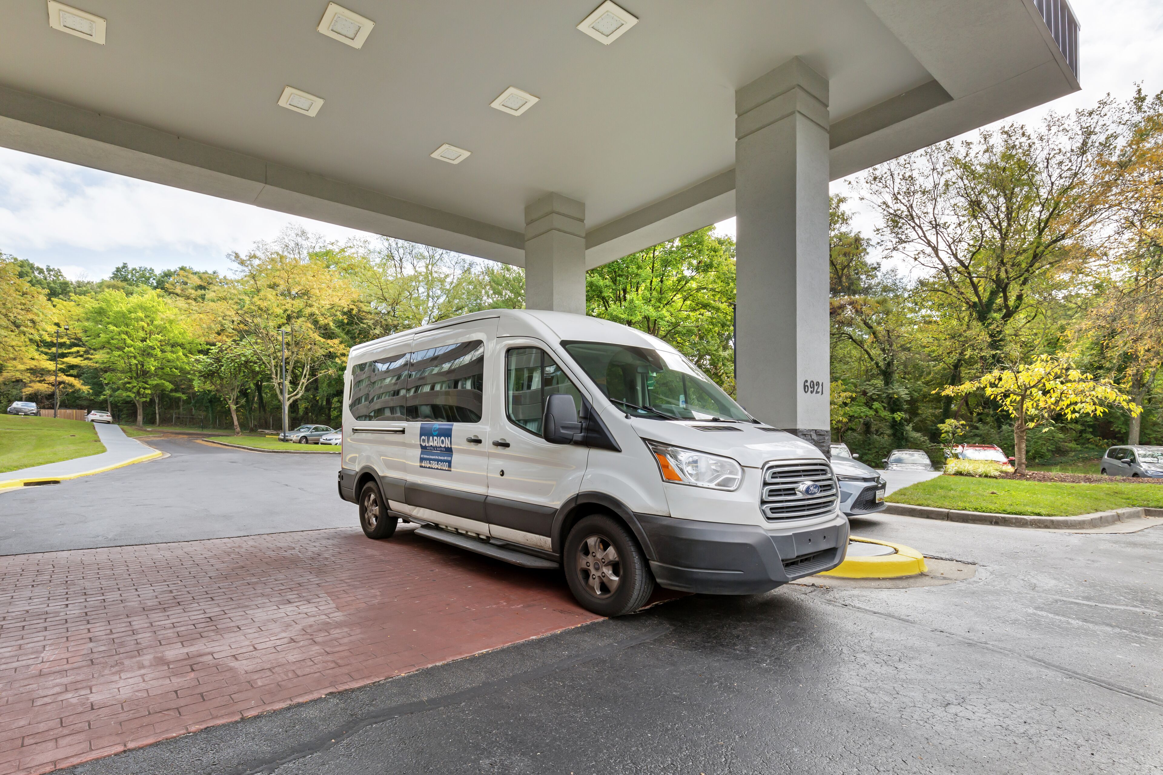 A white van parked at a gas station with a brick-paved area and trees in the background.