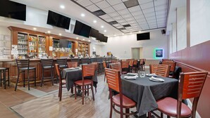 A restaurant with multiple tables and chairs, a bar area with shelves of bottles, and two flat-screen TVs mounted on the ceiling.