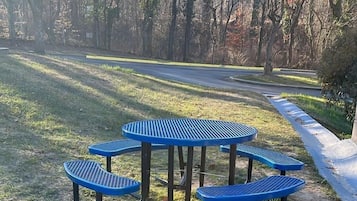 A picnic area with four blue metal tables and benches, surrounded by grass and trees.