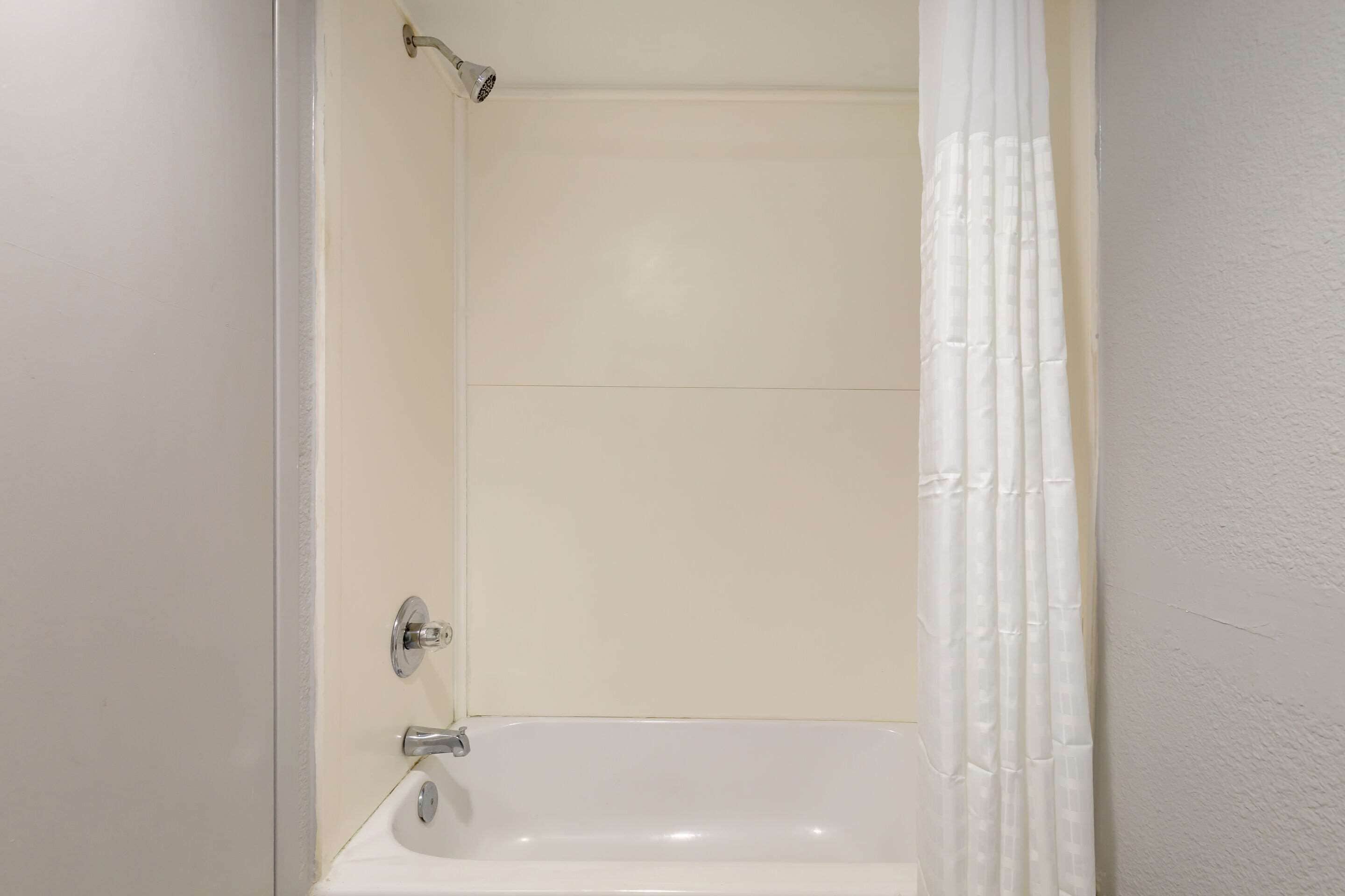 A bathroom with a white bathtub, a shower curtain, and a white wall.