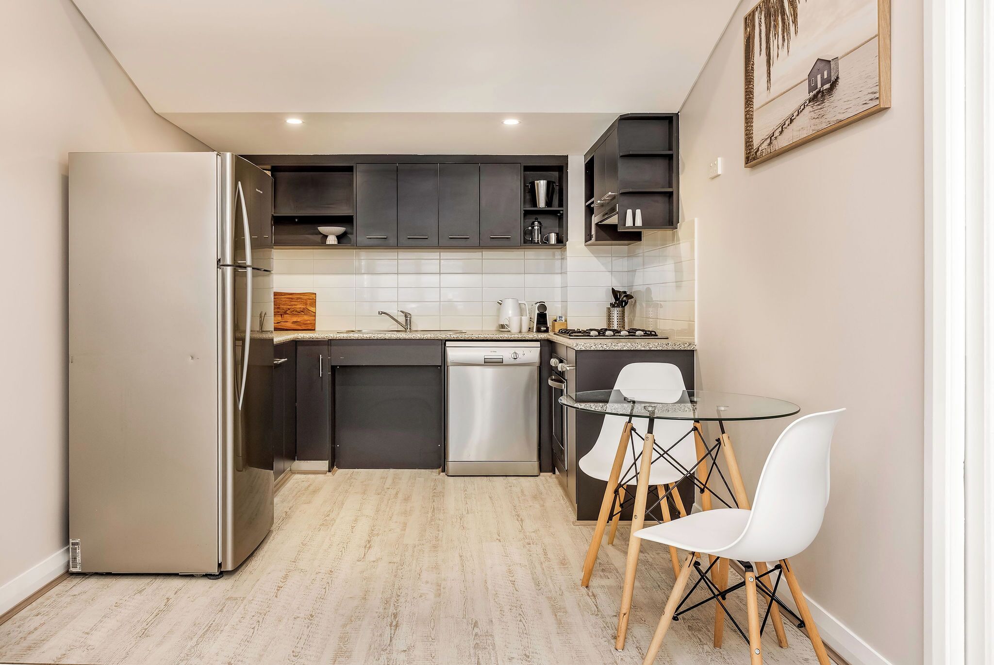 Une cuisine compacte équipée d’un réfrigérateur, d’un lave-vaisselle et d’un petit coin repas avec une table et des chaises.
