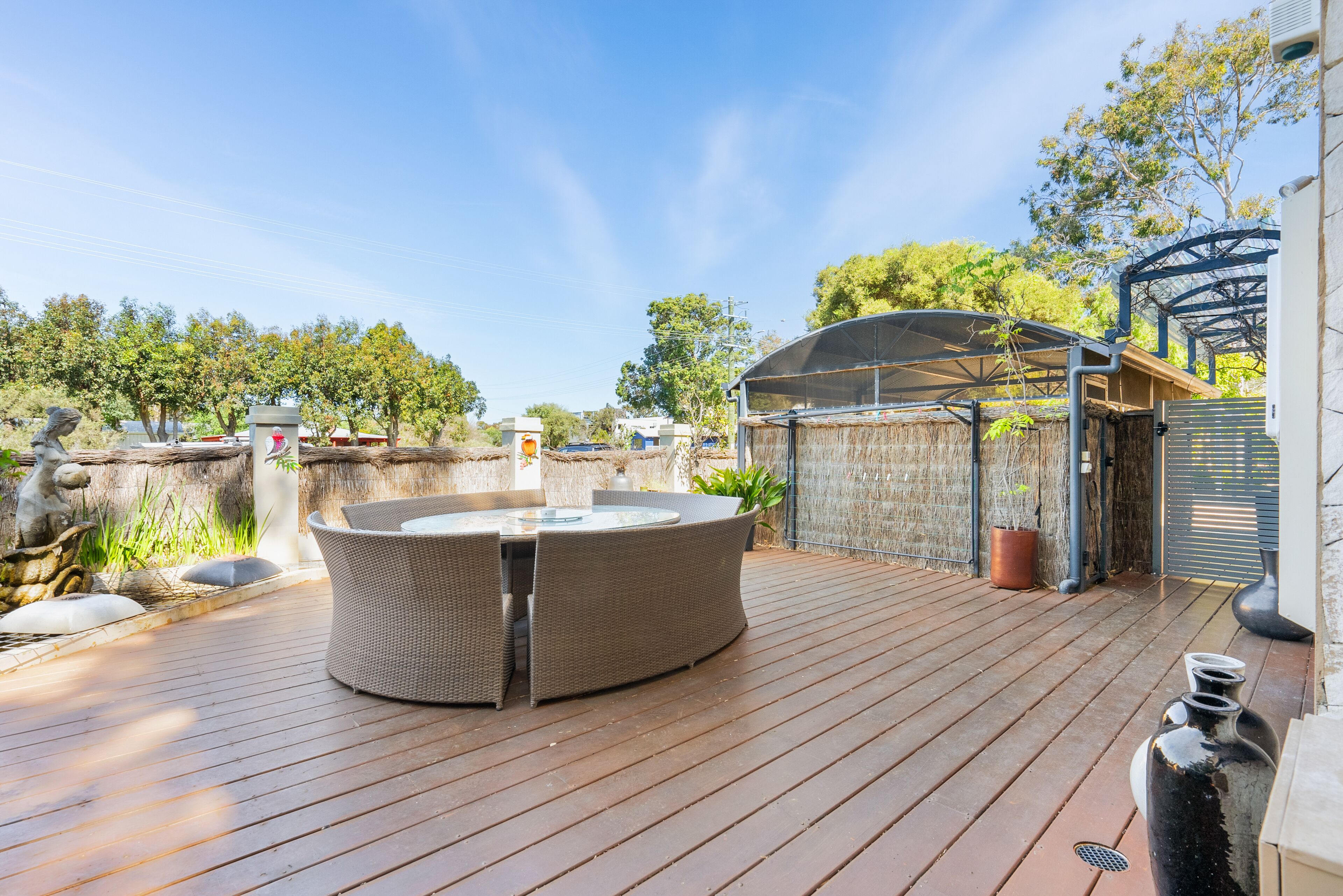 A wooden deck with a round table and chairs, a covered seating area, and a fenced garden.