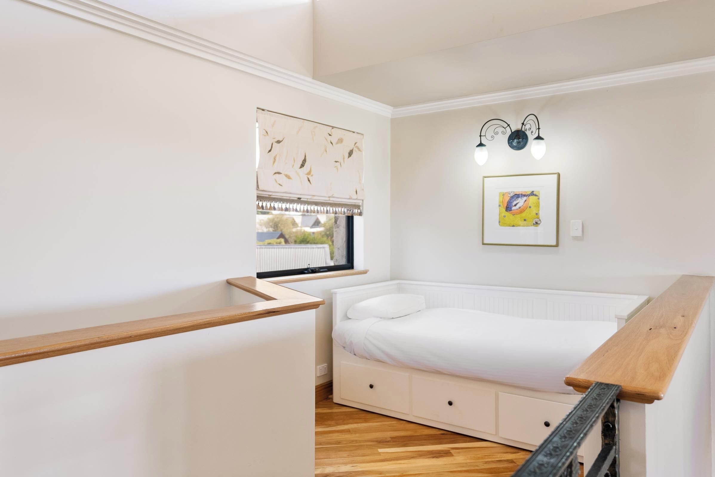 Un dormitorio con una cama, una ventana con persianas, una lámpara fijada a la pared y un banco de madera.