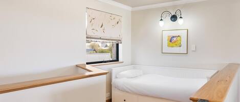 Un dormitorio con una cama, una ventana con persianas, una lámpara fijada a la pared y un banco de madera.