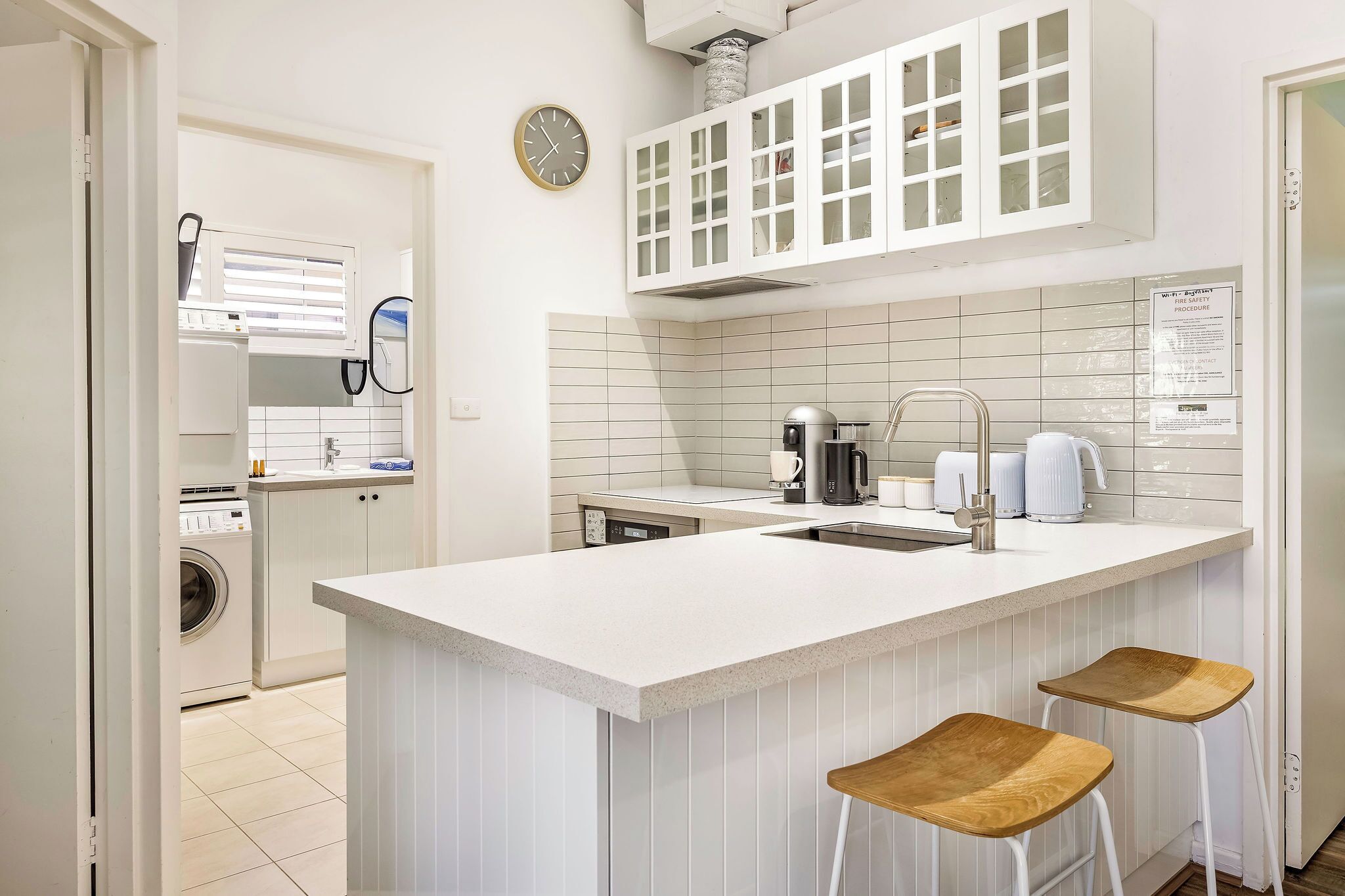 A kitchen with a central island, bar stools, a washing machine, and a clock.