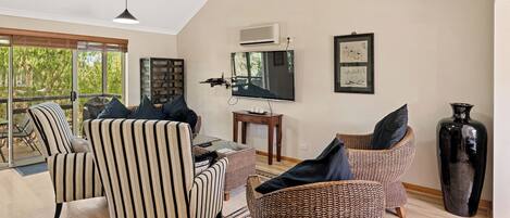 Un salon spacieux avec une grande télévision, des fauteuils à rayures, des canapés en osier et un ventilateur de plafond.