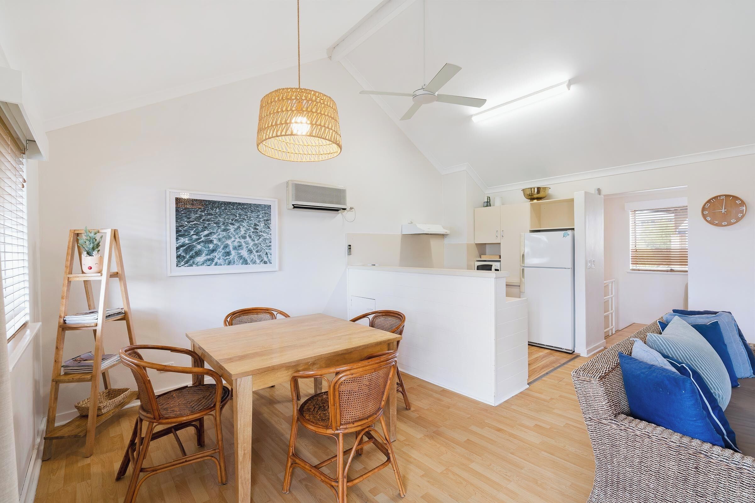 Una cocina moderna con armarios blancos, una mesa de comedor de madera con sillas de mimbre y un ventilador de techo.