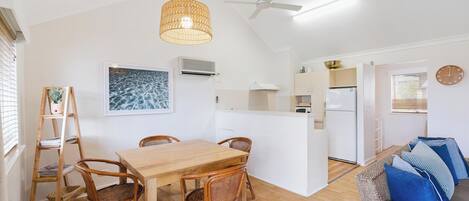 Una cocina moderna con armarios blancos, una mesa de comedor de madera con sillas de mimbre y un ventilador de techo.